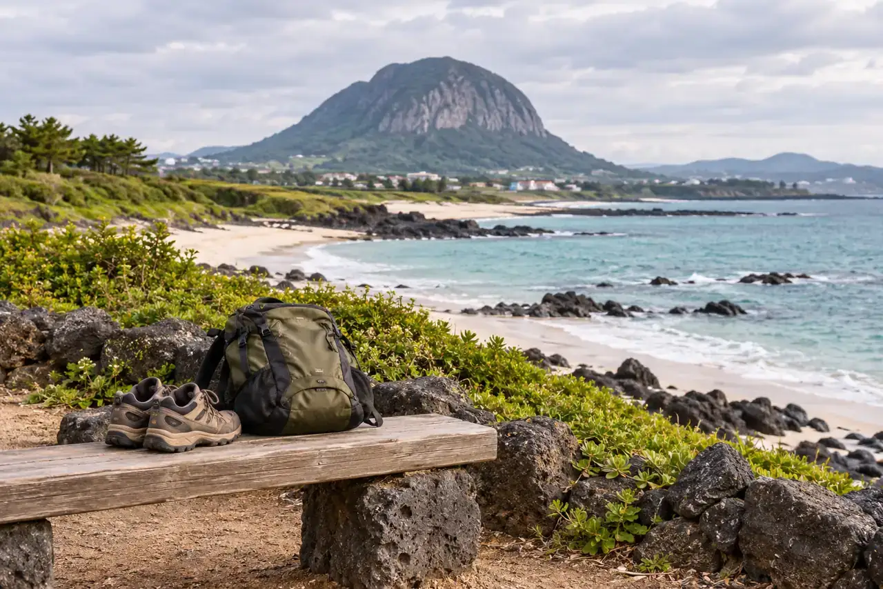 Walking shoes and a daypack on a bench beside the basalt coast, with Sanbangsan in the distance near Hwasun, Jeju.